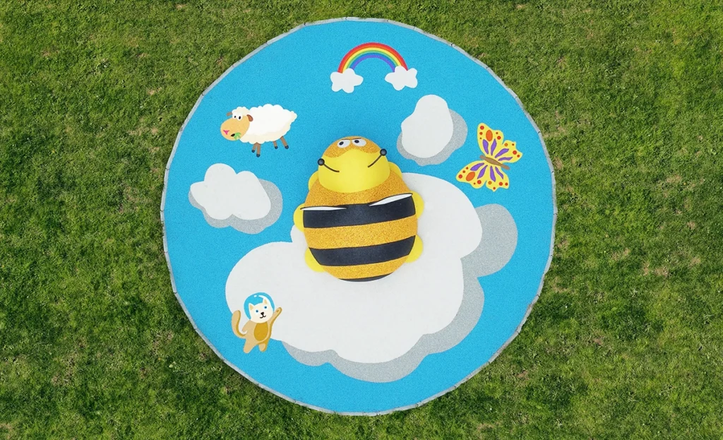 Aerial view of a playground mat featuring a bee on clouds, with illustrations of a sheep, butterfly, rainbow, and monkey on a grassy background.